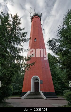 Hel, Polonia - 08.01.2021: Primo piano colpo verticale del faro rosso di Hel contro un drammatico cielo nuvoloso, con alcuni alberi nella parte anteriore. Foto Stock