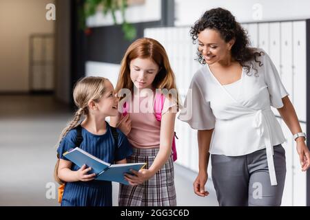 sorridendo insegnante afroamericano che cerca in taccuino nelle mani della scolgirl Foto Stock