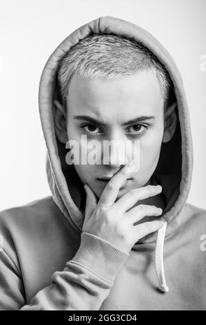 Giovane donna in ocra cappuccio copre il suo volto con mano su sfondo bianco. Monocromatico Foto Stock