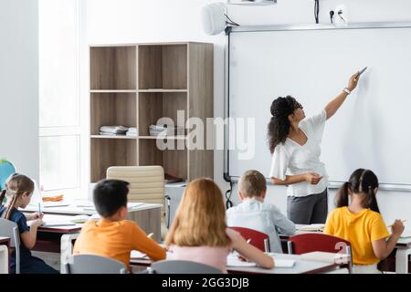 insegnante afroamericano che punta con la penna del feltro alla lavagna durante la lezione Foto Stock