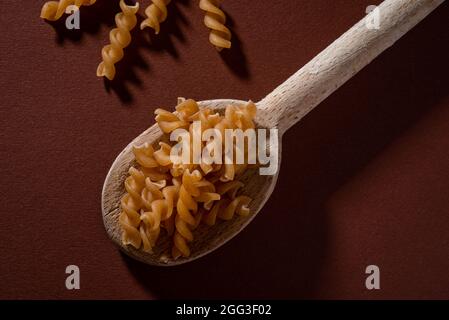Intero pasto Fusilli in cucchiaio di legno su sfondo scuro. Foto Stock