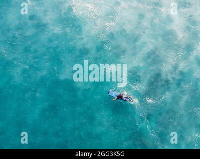 Vista aerea del surfista a bordo di una tavola nell'oceano blu con schiuma dopo l'onda. Vista dall'alto Foto Stock