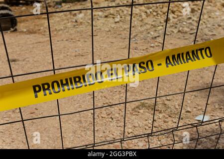 Primo piano di un nastro giallo che avverte della presenza di amianto in un'area urbana e che impedisce ai passanti di uscire dal cantiere con la tex Foto Stock