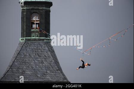 Hohnstein, Germania. 28 agosto 2021. Un runner slackline è appeso su una corda tra il castello e la chiesa cittadina della città in Sassonia Svizzera al Highline - e Family Festival. La linea di allentamento si estende a 30 metri sopra il mercato per oltre 100 metri. Un totale di 4 corde sono installate intorno al castello Hohnstein, la più lunga è di 360 metri sul Polenztal. Credit: Robert Michael/dpa-Zentralbild/dpa/Alamy Live News Foto Stock