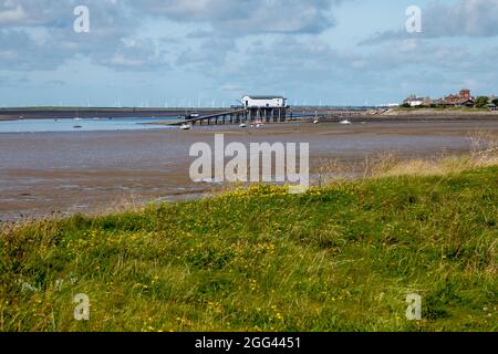 Isola di Roa sulla penisola di Furness, con lo scivolo e la costruzione per la stazione di salvagente di Rnli Barrow e un windfarm in lontananza Foto Stock