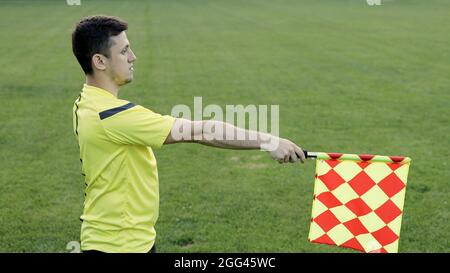 Assistente arbitro che si muove lungo il margine durante una partita di calcio. Mano Linesman con segnalazione bandiera per trappola esterna all'arbitro durante la partita di calcio Foto Stock