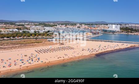 Vista aerea della lussuosa spiaggia di Falesia a Vilamoura. Con i turisti che prendono il sole sui lettini. Porto di Marina con yacht, sullo sfondo. Foto Stock