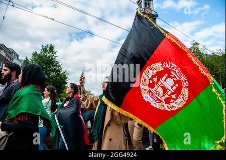 Amsterdam, Paesi Bassi. 28 agosto 2021. Durante la manifestazione, un manifestante detiene una bandiera afghana.migliaia di persone si sono riunite nel centro di Amsterdam per dimostrare il loro sostegno alla popolazione afghana intrappolata a Kabul sotto il regime talebano e per esortare il governo olandese a dichiarare l'Afghanistan un paese di origine non sicuro così come i rifugiati afghani e. Le persone afghane senza documenti possono avere il diritto legale di asilo e sicurezza. (Foto di Ana Fernandez/SOPA Images/Sipa USA) Credit: Sipa USA/Alamy Live News Foto Stock