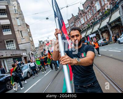 Amsterdam, Paesi Bassi. 28 agosto 2021. Durante la manifestazione, un manifestante detiene una bandiera afghana.migliaia di persone si sono riunite nel centro di Amsterdam per dimostrare il loro sostegno alla popolazione afghana intrappolata a Kabul sotto il regime talebano e per esortare il governo olandese a dichiarare l'Afghanistan un paese di origine non sicuro così come i rifugiati afghani e. Le persone afghane senza documenti possono avere il diritto legale di asilo e sicurezza. (Foto di Ana Fernandez/SOPA Images/Sipa USA) Credit: Sipa USA/Alamy Live News Foto Stock