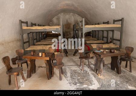 Dinant, Vallonia, Belgio - 8 agosto 2021: Forte Cittadella. Dormitori sotto bastioni per soldati con letti a castello, sedie e tavoli. Fila di fucl Foto Stock