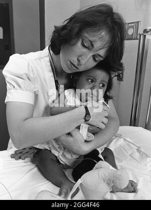 Austin Texas USA, circa 1989: L'infermiera nell'ospedale dei bambini abbraccia il paziente giovane sull'esame del tavolo per calmarla. ©Bob Daemmrich Foto Stock