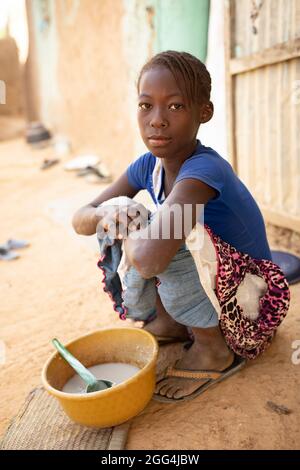 Una ragazza mangia una ciotola di porridge di miglio per colazione fuori dalla sua casa di villaggio nella regione di Ségou, Mali, Africa occidentale. Foto Stock