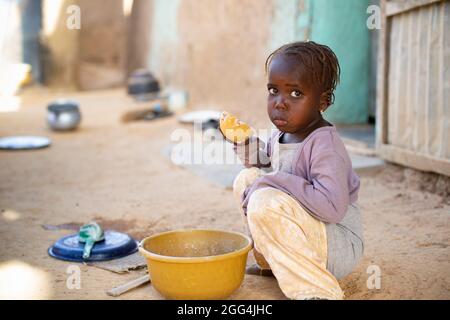 Una ragazza mangia una ciotola di porridge di miglio per colazione fuori dalla sua casa di villaggio nella regione di Ségou, Mali, Africa occidentale. Foto Stock