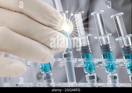 Un uomo che regge una siringa di vetro con effetti di luce incandescente e luce soffusa l'immagine di con diverse siringhe preriempite con liquido blu su un rack. Foto Stock