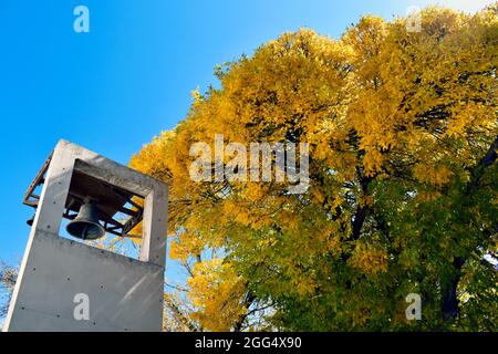 chiesa torre con campana di bronzo e alberi con foglie di autunno giallo e cielo blu sullo sfondo Foto Stock