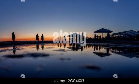 Sagome di una grande folla di gente al bar sul mare durante il tramonto con riflessi nell'acqua Foto Stock