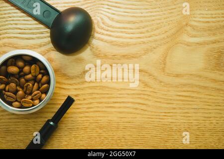 Chicchi di caffè in ciotola d'argento e utensil nero su sfondo di legno con spazio copia Foto Stock