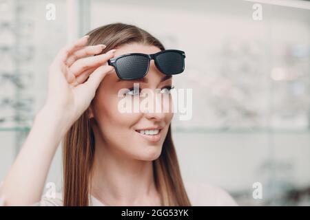 Giovane Donna con occhiali neri punzonati per l'allenamento visivo. Trainer per occhiali perforati. Foto Stock