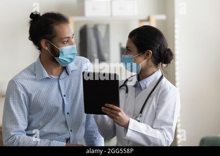 Focalizzato giovane paziente di razza mista e medico di discussione sul trattamento della malattia. Foto Stock