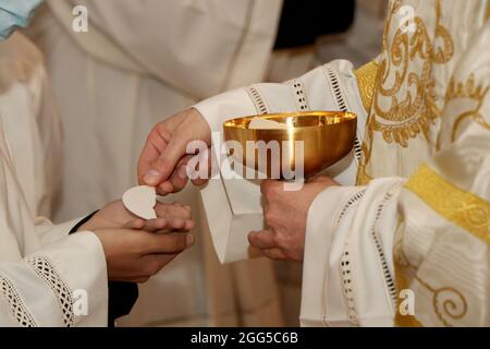 Rito di comunione durante la messa in una chiesa cattolica. Il sacerdote dà l'ospite nelle mani di un fedele Foto Stock