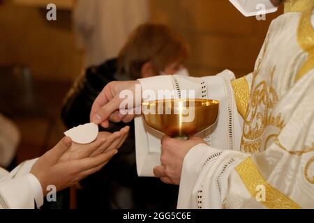 Rito di comunione durante la messa in una chiesa cattolica. Il sacerdote dà l'ospite nelle mani di un fedele Foto Stock