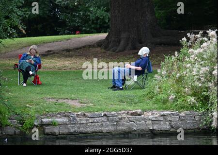 Un uomo e una donna si rilassano in sedie pieghevoli sulle rive del fiume Avon vicino al centro della città di Stratford upon Avon, Warwickshire. L'uomo è vestitore Foto Stock