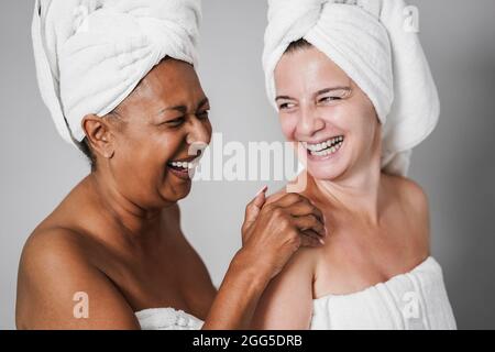 Donne anziane multirazziali con pelle e corpo diversi ridendo insieme mentre indossano gli asciugamani per il corpo - fuoco principale sul viso femminile africano Foto Stock