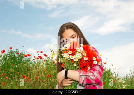Bouquet di fiori selvatici: Papaveri, margherite in mano contro il cielo blu. Fiori in mano di una donna Foto Stock