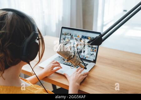 Podcaster femminile che registra il suo podcast utilizzando il microfono e il portatile presso il suo studio di trasmissione a casa. Donna in streaming dal vivo da casa studio radio Foto Stock