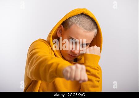 Giovane donna in cappa ocra che tiene i pugni vicino faccia su sfondo bianco. Foto Stock