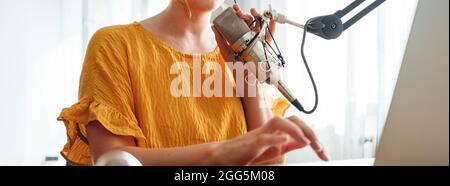 Donna radio ospite di registrare e trasmettere il suo podcast da casa studio. Il podcaster femmina parla nel microfono sul tavolo. Immagine ampia. Primo piano Foto Stock