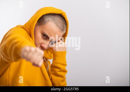 Giovane donna in cappa ocra che tiene i pugni vicino faccia su sfondo bianco. Boxer girl è pronta per una lotta. Foto Stock