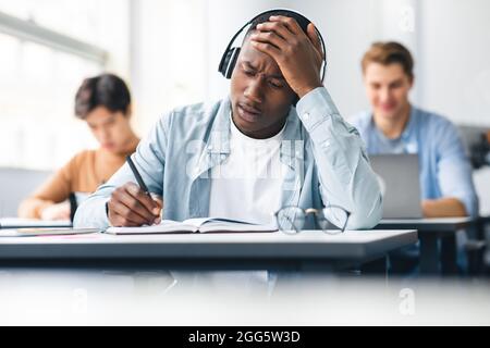 Scioccato nero studente iscritto prova seduta alla scrivania in classe Foto Stock