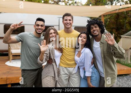 Ritratto di diversi giovani amici in posa e sorridenti a macchina fotografica vicino al rimorchio, godendo il fine settimana autunnale in campeggio Foto Stock