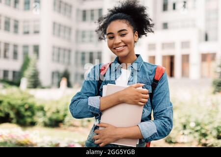 Felice ragazza americana dell'adolescente che posa vicino all'edificio moderno dell'università Foto Stock