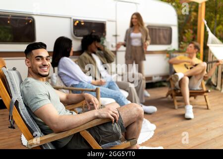 Gruppo di giovani amici multirazziali che hanno partito all'aperto vicino camper van, suonare la chitarra, divertirsi in vacanza autunno Foto Stock