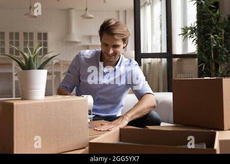 Sorridente giovane uomo che confezionano oggetti in scatole di cartone. Foto Stock