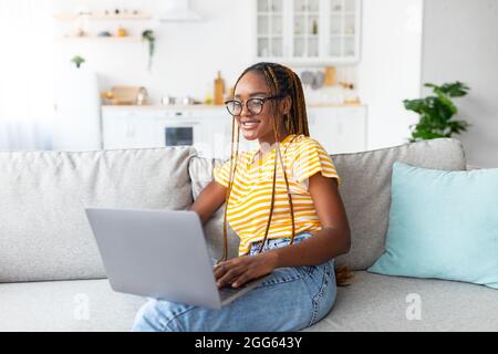 Positivo afroamericana donna seduta sul divano, utilizzando il portatile Foto Stock