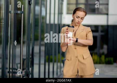 Bella giovane donna d'affari caucasica carina con tazza di caffè, utilizzando il telefono cellulare e bere caffè sorridente. Foto Stock
