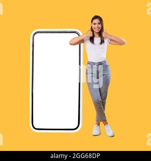 Donna che mostra lo schermo bianco vuoto dello smartphone e pollici in alto Foto Stock