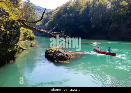 Veduta aerea di madre e figlio che remano in una canoa rossa sul fiume Soca sotto un vecchio ponte di pietra vicino a Most na Soi, Avce, Slovenia Foto Stock