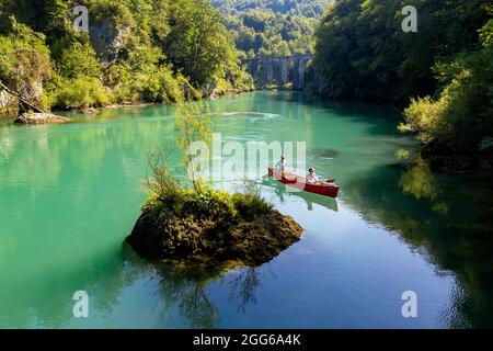 Veduta aerea di madre e figlio che remano in una canoa rossa sul fiume Soca sotto un vecchio ponte di pietra vicino a Most na Soi, Avce, Slovenia Foto Stock