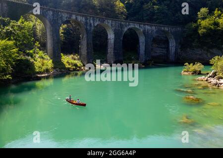 Veduta aerea di madre e figlio che remano in una canoa rossa sul fiume Soca sotto un vecchio ponte di pietra vicino a Most na Soi, Avce, Slovenia Foto Stock