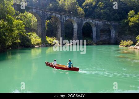 Veduta aerea di madre e figlio che remano in una canoa rossa sul fiume Soca sotto un vecchio ponte di pietra vicino a Most na Soi, Avce, Slovenia Foto Stock