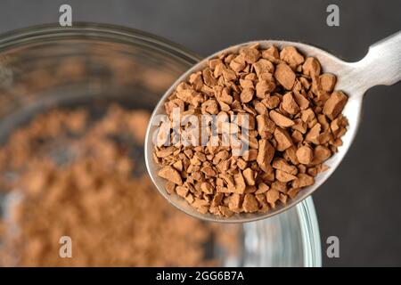 Congelare il caffè istantaneo essiccato su cucchiaino da tè con fondo tazza di caffè in vetro. Foto Stock