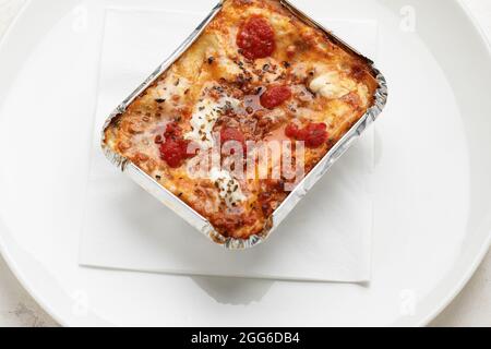 Togliere la lasagna cremosa con mozzarella fresca e pomodori sul piatto bianco con tovagliolo Foto Stock