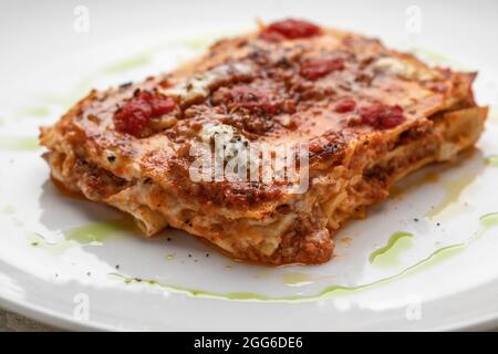 Togliere la lasagna cremosa con mozzarella fresca e pomodori sul piatto bianco macro close up Foto Stock