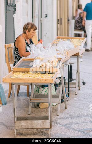 Donna anziana locale che si prepara per la strada della città vecchia di Bari orecchiette o orecchietta, fatta con grano duro e acqua, pasta fatta a mano di Pugllia Foto Stock