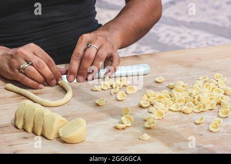 Mani di donna che si preparano per la via delle orecchiette o orecchiette del centro storico di Bari, fatte con grano duro e acqua, pasta fatta a mano tipica della Puglia Foto Stock