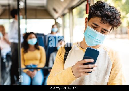 Ragazzo asiatico in maschera utilizzando il telefono in autobus Foto Stock